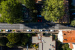 © Aerial Film Studio - Aerial view of a straight street in Grasse, France with zebra crossing, terracotta and flat roofs, parked cars, side lane to a shaded courtyard in mid day sun.
