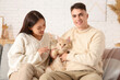 © Pixel-Shot - Beautiful young couple with cute Maine Coon cat sitting on sofa in living room
