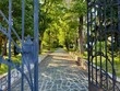 © Milena - Open old metal gate in front of a tree lined stone path in a church yard in the afternoon sun in Zagreb, Croatia