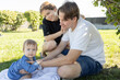 © Anna - Portrait of happy young parents having fun with their baby girl in the park, sitting on the grass. Loving family of three of Caucasian descent enjoying time together. Lifestyle. Family day.