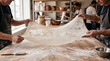 © Bernardo - Hands stretching translucent thin filo pastry dough over table.
