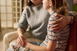 © Mediaphotos - Caucasian mother comforting teenage daughter while holding hands and embracing shoulder during serious home conversation, representing parental support. Useful for family counseling campaigns