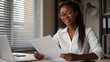 © AZ Studio - Young Black woman in glasses reviewing documents at her desk with a laptop