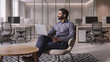 © insta_photos - Young thoughtful bearded smart indian professional business man executive looking away sitting on chair in modern office lobby using laptop, thinking of new ideas, planning project, working online.