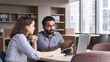 © insta_photos - Professional indian teacher, executive or mentor helping latin student, new employee, teaching intern, explaining online job using laptop computer, talking, having teamwork discussion in office.