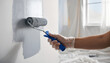 © Alex & M Studio - Close up view of hand in transparent glove applying grey paint to white wall using small paint roller during interior home decoration and room makeover process in bright modern apartment space