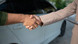 © NanSan - Close-up handshake between two people next to a white car, suggesting agreement during vehicle sale or service transaction, outdoor daylight, shallow depth of field.