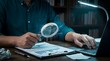 © Sana - audit, documents, magnifying, glass, verification, Close-up of a person using a magnifying glass to inspect documents beside a laptop, representing auditing, verification, and detailed analysis.