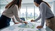 © Emma - Two business women architects discussing solar panel blueprint plans on table, sustainable energy project design, renewable power plant construction meeting