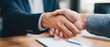 © sam richter - An impactful close-up view of two professionals locking hands over paperwork in a corporate environment, symbolizing trust, agreement, and closing a successful business deal.