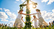 © Elena - Four happy women in white dresses and flower crowns holding hands and dancing around a tall decorated Midsummer pole