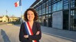 © MUHAMMAD - Smiling young French elected official proudly wearing a ceremonial tricolor sash representing public service outside the local town hall building.