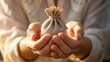 © Dollar - Close-up of hands holding a small burlap drawstring bag for savings or charity concepts