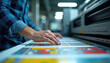 © Vadym - Man aligns color print plates on large format printer. Worker checks registration marks on paper sheets for accurate graphic reproduction. Pro color separation in print shop.