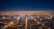 © Budirahayu - Panoramic aerial view of a sprawling modern city at night, showcasing illuminated skyscrapers, urban infrastructure, and glowing streetlights under a dark sky.