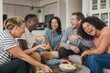 © Natallia Simanchyk - Diverse group of friends sitting around a coffee table, laughing and sharing snacks. They enjoy a fun social gathering in a modern living room. Perfect for lifestyle and community content.
