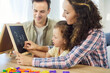 © Studio Romantic - Family parents guide daughter writing numbers and alphabet. At home, child girl learning on a chalkboard as parents guide, making education and homework easier. Supportive education and development.