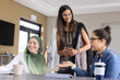 © wavebreak3 - Diverse female coworkers standing and discussing around meeting table at office with laptop