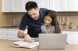 © fizkes - Caring young father helping with school assignment or essay to his little adorable daughter, sit at table in kitchen read textbook, doing tasks or making tests together. Tuition, education, knowledge