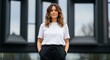 © udiana - Confident woman in casual white t-shirt and black sweatpants standing outdoors with modern building background