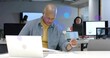 © vectorfusionart - Reviewing bald man in shirt typing on laptop, scanning documents at open office with monitors