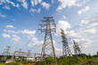 © tai - Multiple steel lattice transmission towers and power lines stand in a grassy field under a blue cloudy sky, part of electrical power infrastructure.