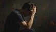 © ruangrit19 - Young man sitting in profile with head in hands looking stressed and overwhelmed with a dark moody background for mental health concept.