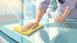 © AS_SleepingPanda - A person uses a yellow cloth to wipe and clean a glass table in a bright room during the day to keep the home clean and tidy