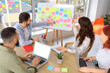 © Pixel-Shot - Group of young people discussing business plan at table with Kanban board in office