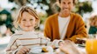 © Pinklife - A cheerful child smiles at the camera while sharing breakfast with an adult, accentuating the joy of family moments in a beautifully set outdoor dining space.