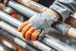 © Kowit - A gloved hand grips a metal pipe, highlighting manual labor and industrial safety.