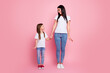 © deagreez - Mother and daughter holding hands and smiling together against a pink background — happy family moment with casual outfits and warm connection