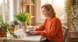 © Vyatcheslav - Young woman working on laptop at home. Happy female freelancer typing on computer in sunlit room with plants