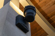 © Michael - Outdoor black sound system speaker or security siren mounted on textured concrete pillar under wooden ceiling with golden hour sunlight.