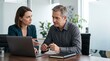 © Eve - Business colleagues discussing project on laptop in modern boardroom. Professional man and woman focused on work during meeting in bright corporate office workspace.