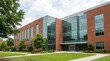 © David - Modern brick building with large glass windows and a contemporary facade, surrounded by green lawns and trees on a bright day.
