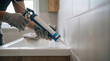 © kodidesign - Worker applying silicone sealant to bathroom tiles. Professional repairman using a caulking gun for home renovation