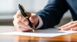 © MopoWe - Fountain pen held by executive signing document on wooden desk with sharp focus and bokeh. Natural light illuminates the workspace. Ideal for legal and financial service marketing.