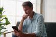 © Tj - Mature man contemplating serious news on smartphone, having concern, uncertainty, and thinking about difficult decisions while using modern technology