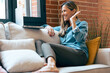 © Westend61 - Woman waving at laptop during video call on couch at home