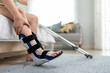 © Kawee - Close up of injured woman wearing splint on leg in cozy bedroom at home.