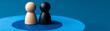 © Yuparet - Wooden figurine in black and natural color stand together on blue target symbolizing challenge idea and strategic disagreement with calm emotional expression