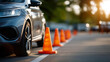 © Denis Yevtekhov - A learner vehicle parked near a line of orange traffic cones on a sunlit training lot, no people, driving school car, traffic cones, practice ground, driver education, training lot, safety