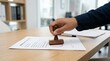 © Anwar - Close-up of a hand stamping a document on a wooden desk in an office setting.