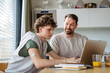 © Halfpoint - Father helping teenage son with diabetes with homework on laptop in kitchen.