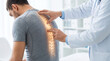 © Taras Roshchuk - A doctor checks the spine of a man who has back pain in a medical clinic. The doctor uses his hand to point at the man's spine. The setting is bright and clean