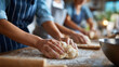 © Nataliya - Close-up of hands kneading dough at a group baking workshop with aprons visible, culinary hobby concept, bread making class, teamwork in kitchen, defocused background, with copy
