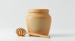 © E Faysal - A wooden honey jar with a honey dipper on a white surface indoors.