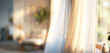 © Wisnu - A softly lit interior scene showcasing sheer curtains, creating a warm ambiance with blurred furniture and greenery in the background.
