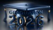 © www.freund-foto.de - Dunkelblauer dreidimensionaler Schriftzug „Graduation 2026' mit goldenem Akzent auf einer Podestfläche mit Doktorhut auf dunklem Hintergrund